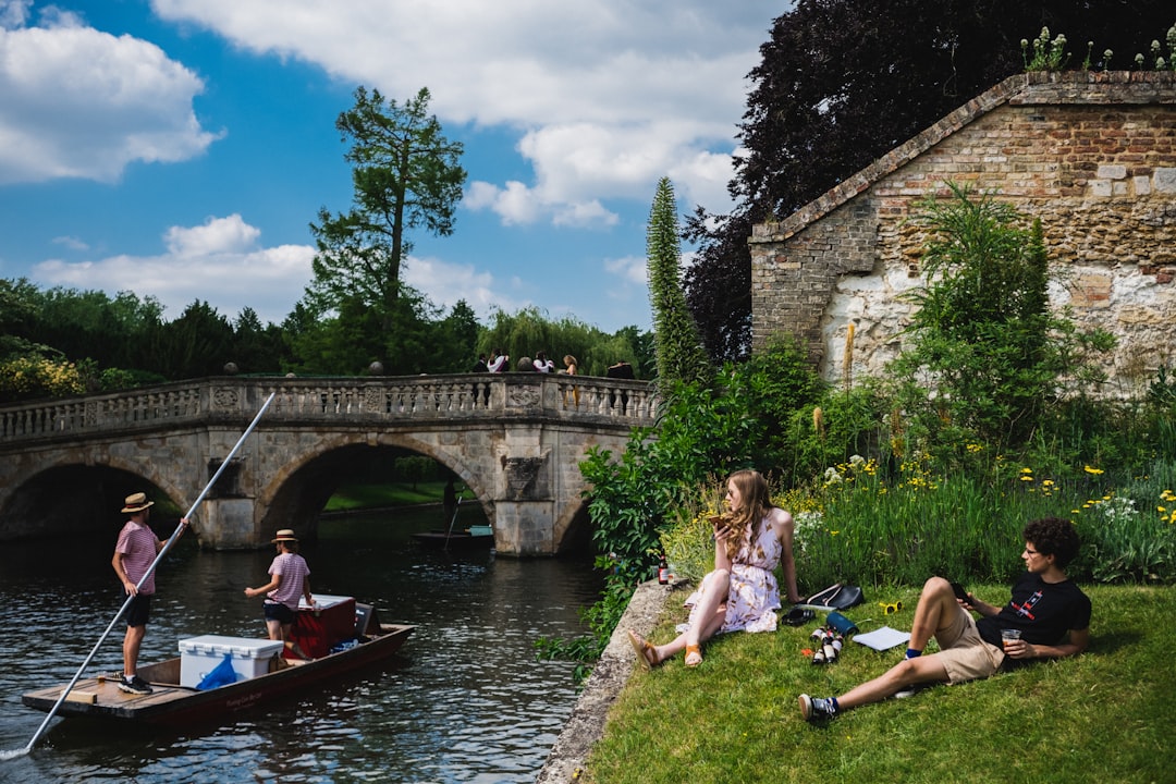 Cambridge, Cambridgeshire: a group of people sitting on the side of a river next to a bridge
